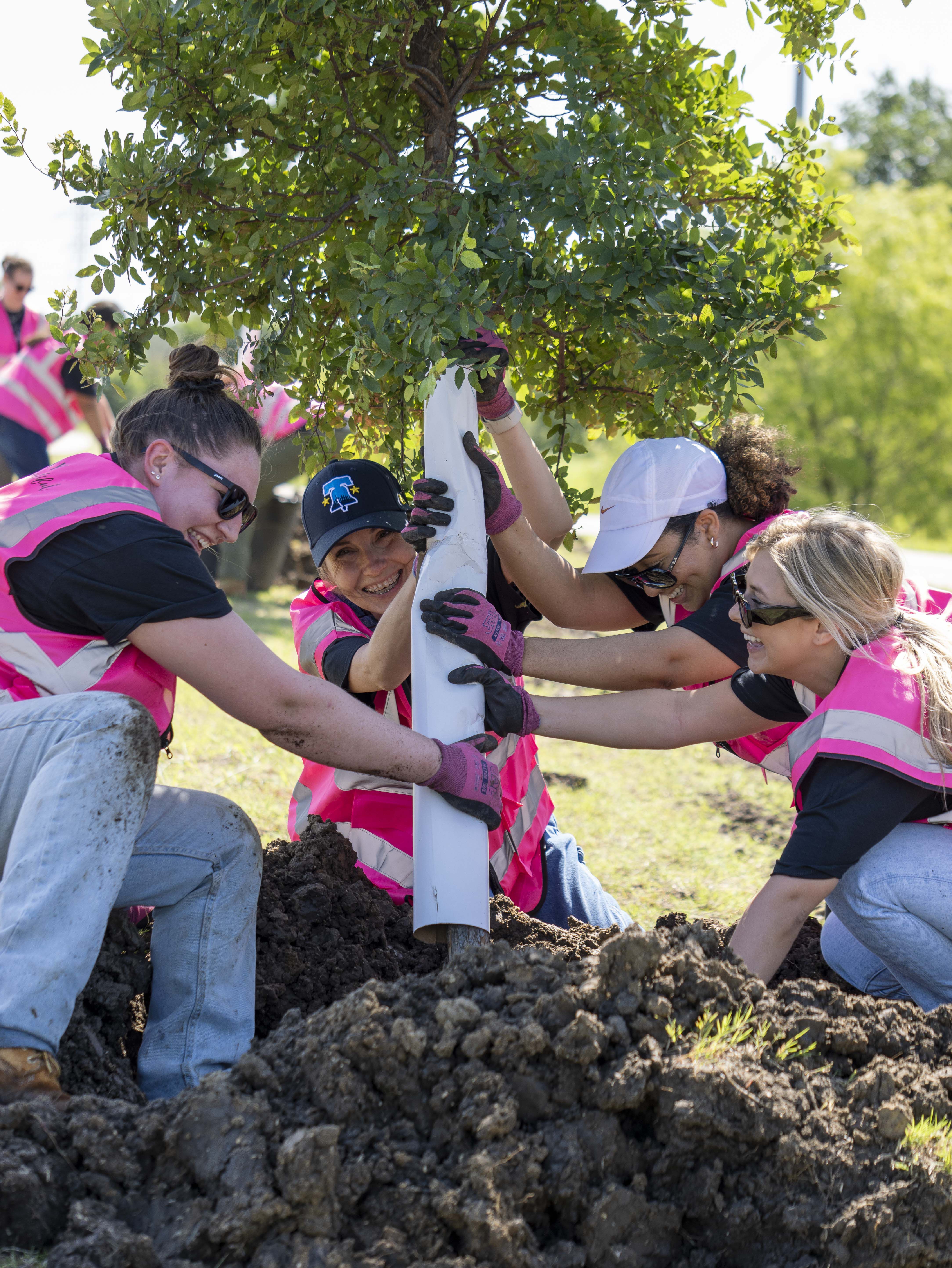Team members wearing pink vests working together to plant a tree, Mary Kay.